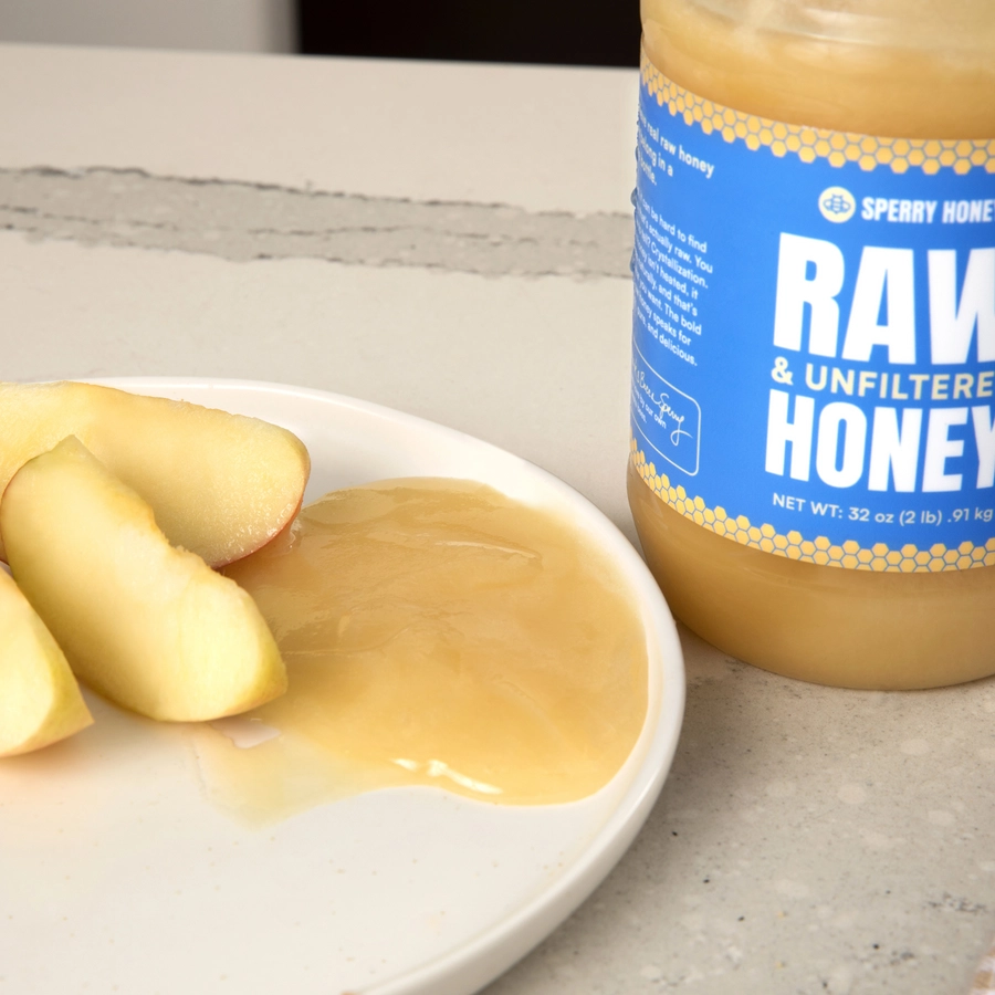 Sperry Raw Honey jar with honey on a plate of apples on a light surface
